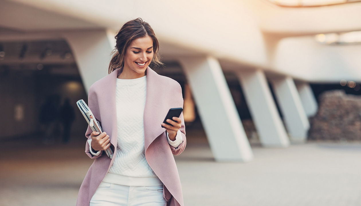 woman in pink coat smiling looking into phone